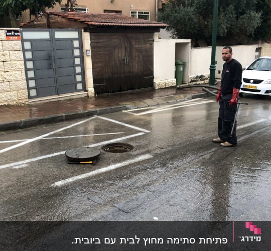 אדם ליד פתח ביוב פתוח בכביש רטוב